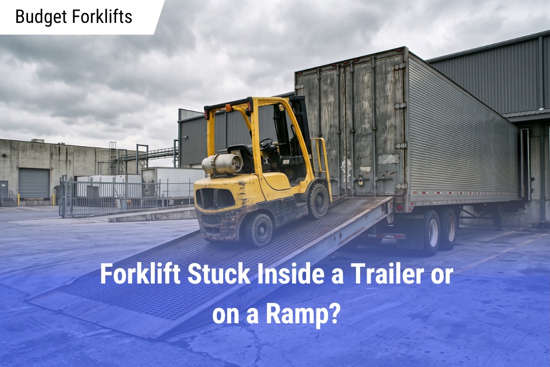 A yellow warehouse forklift stuck partway up a metal loading ramp leading into a closed box trailer at an industrial dock.